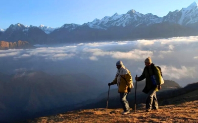 Two hikers walking on a ridge above the clouds with the Panchachuli peaks visible in Munsiyari